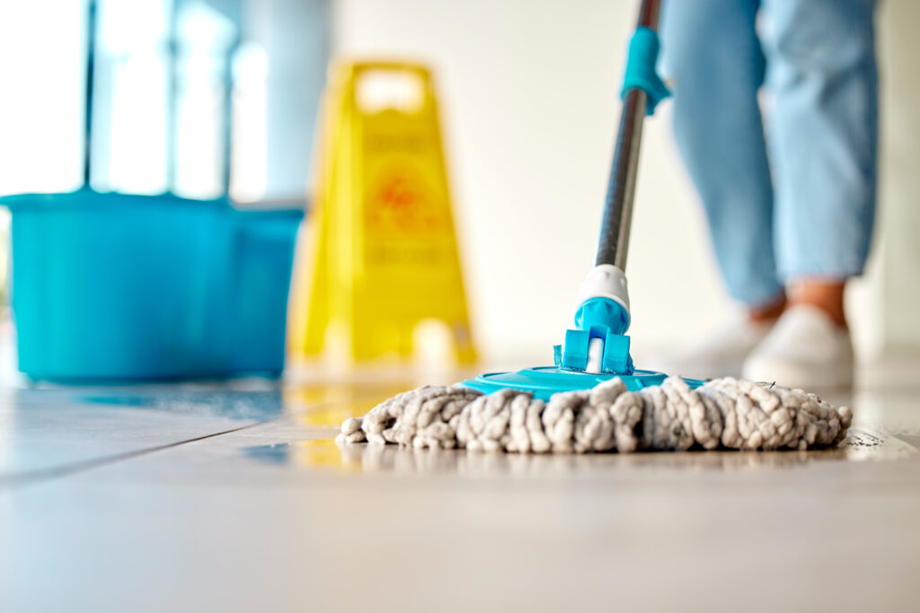 A person mops the floor using a range of janitorial equipment in an aged care or healthcare setting.