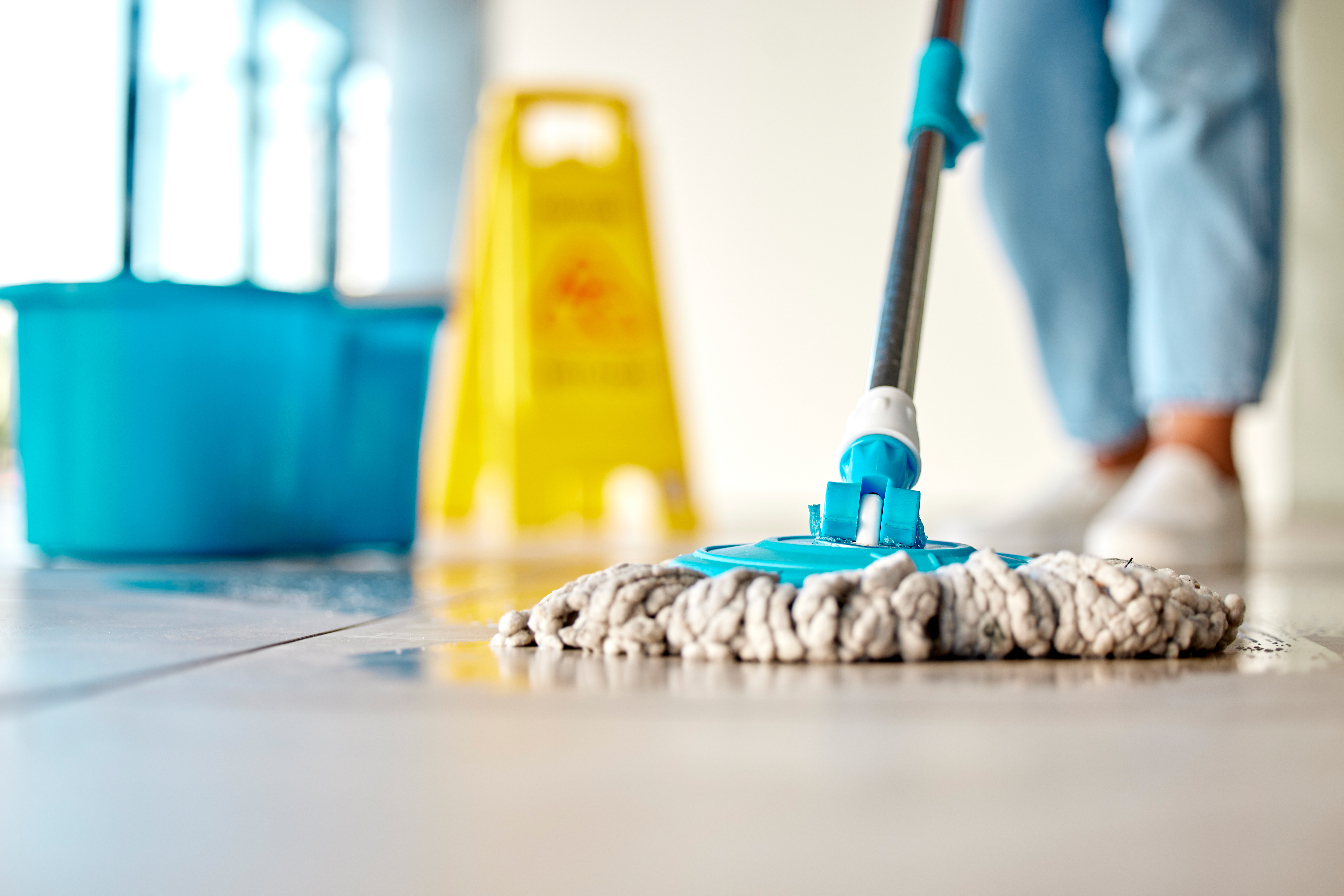 A person mops the floor using a range of janitorial equipment in an aged care or healthcare setting.