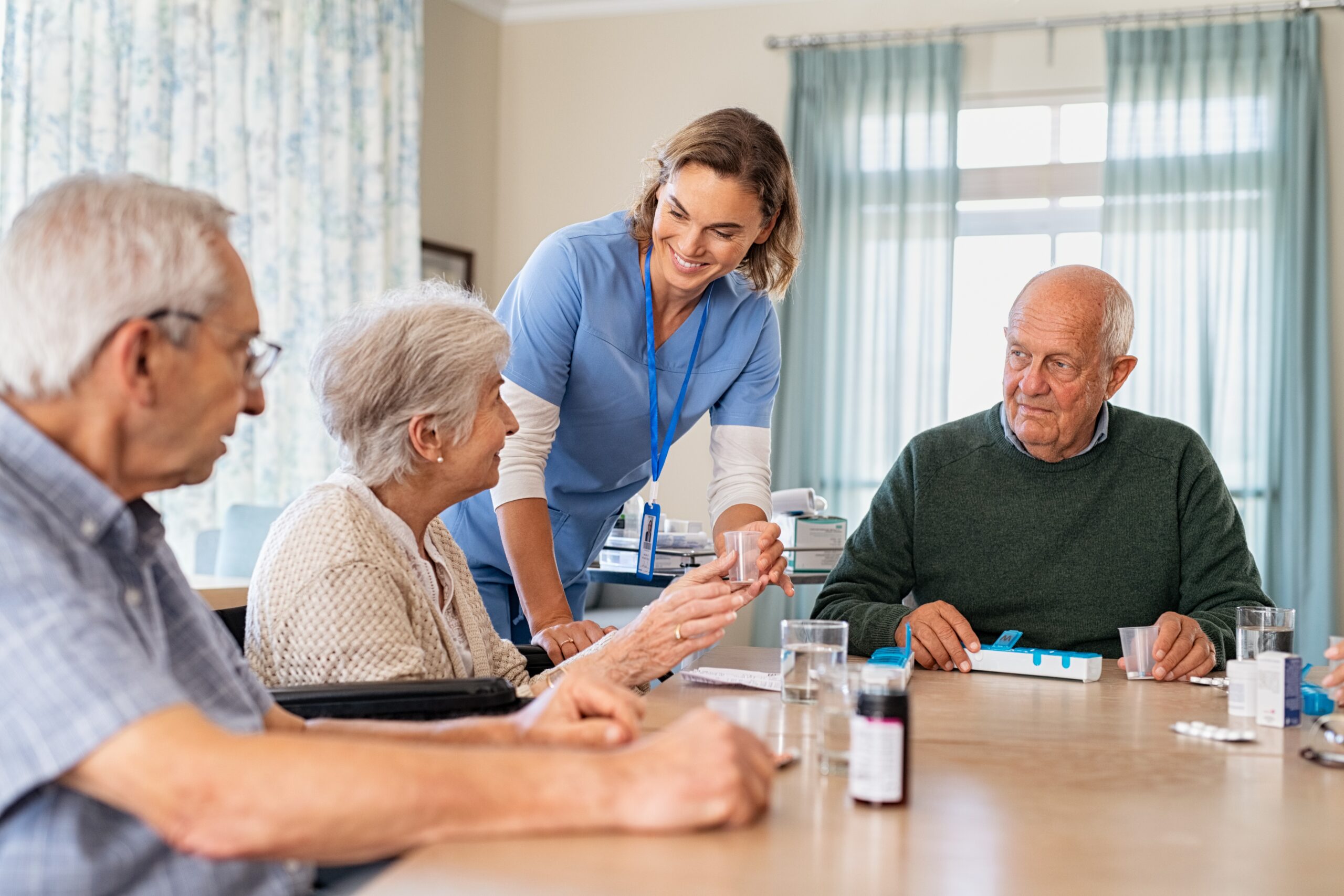 A group of residents at an Aged Care setting are given their medication by a nurse.